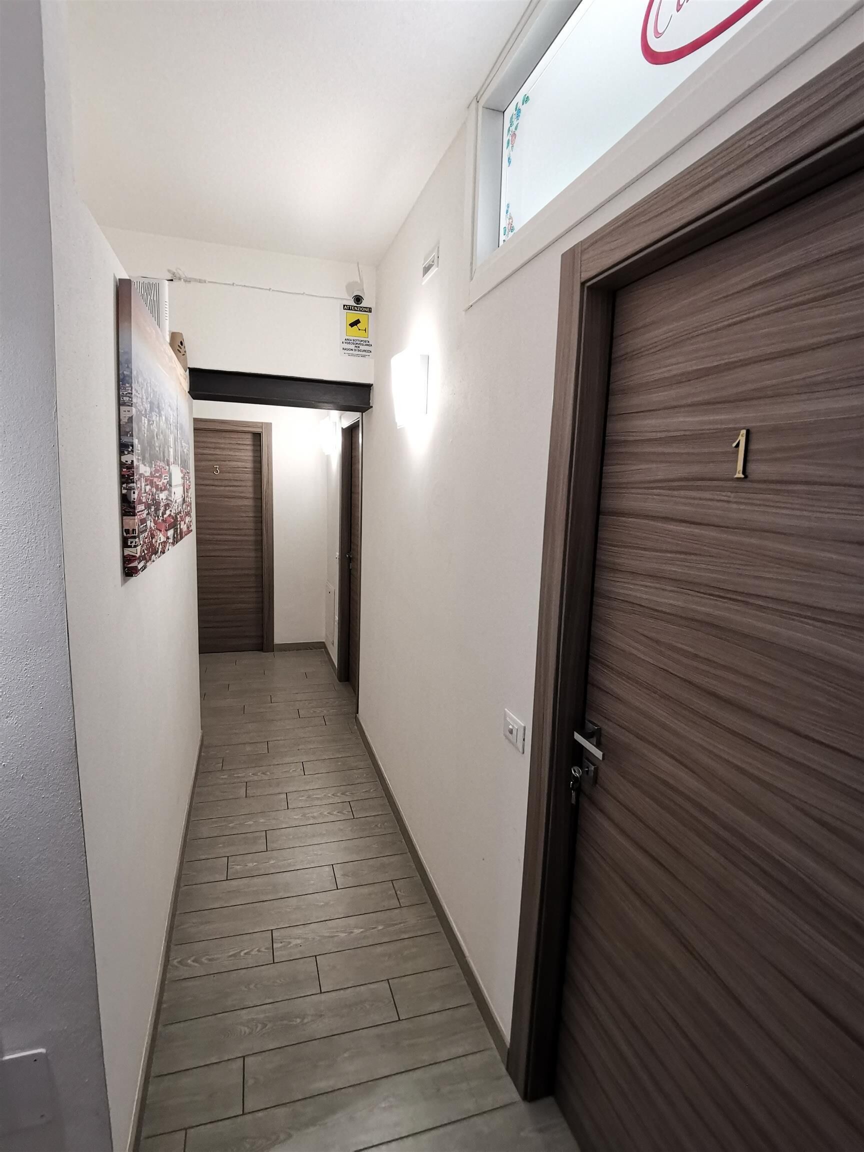 A hallway with a wooden door labeled '1', a wall-mounted sign, and a poster.