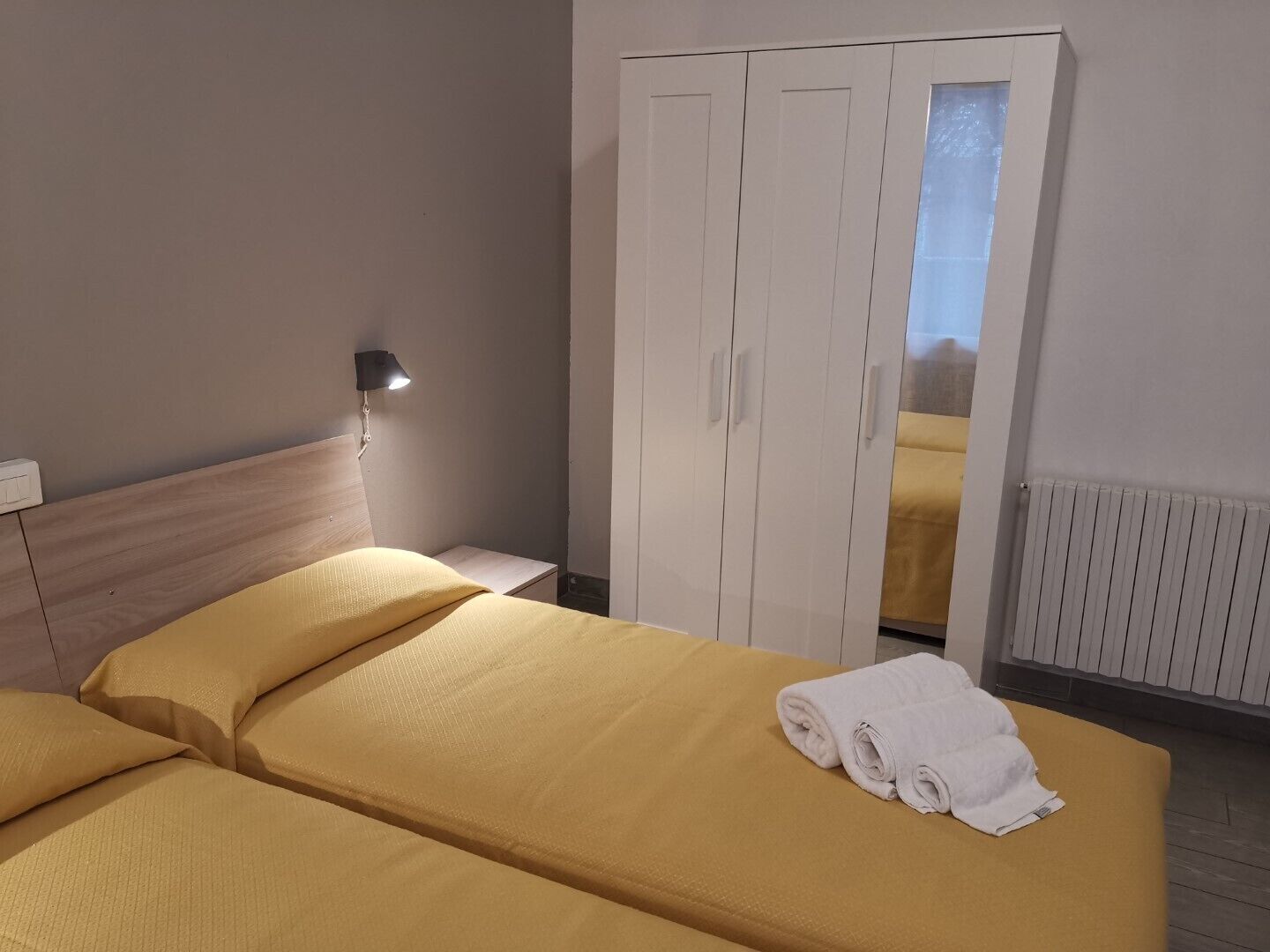 A hotel room with two beds, a wardrobe, a nightstand, and a lamp.