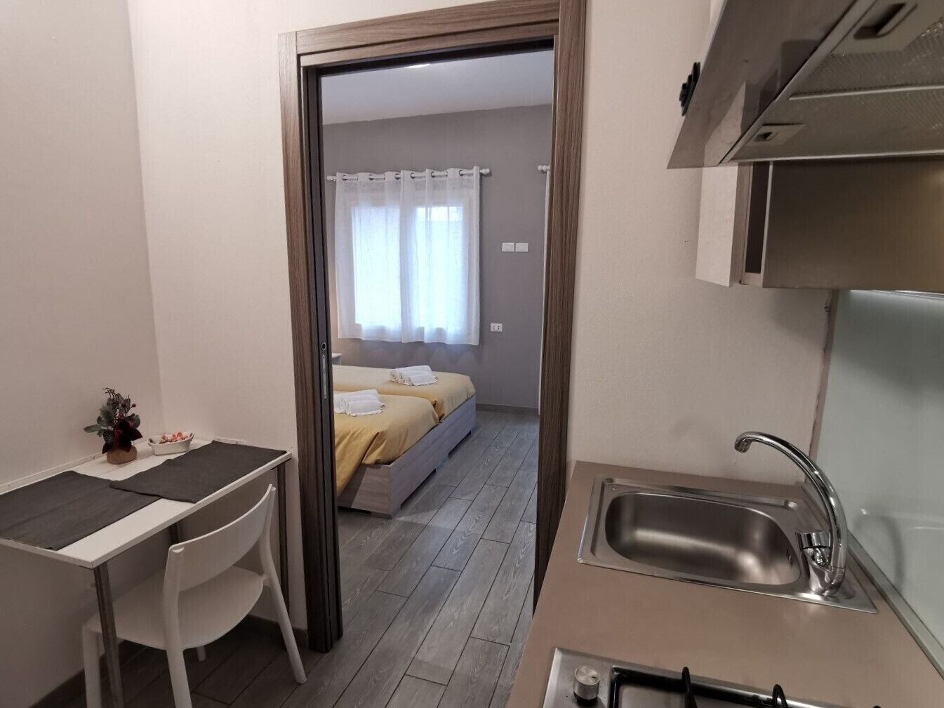Une chambre d’hôtel compacte comprenant un coin cuisine, un lit avec une literie blanche et un petit espace salon avec une table et une chaise.