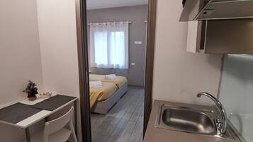 Une chambre d’hôtel compacte comprenant un coin cuisine, un lit avec une literie blanche et un petit espace salon avec une table et une chaise.
