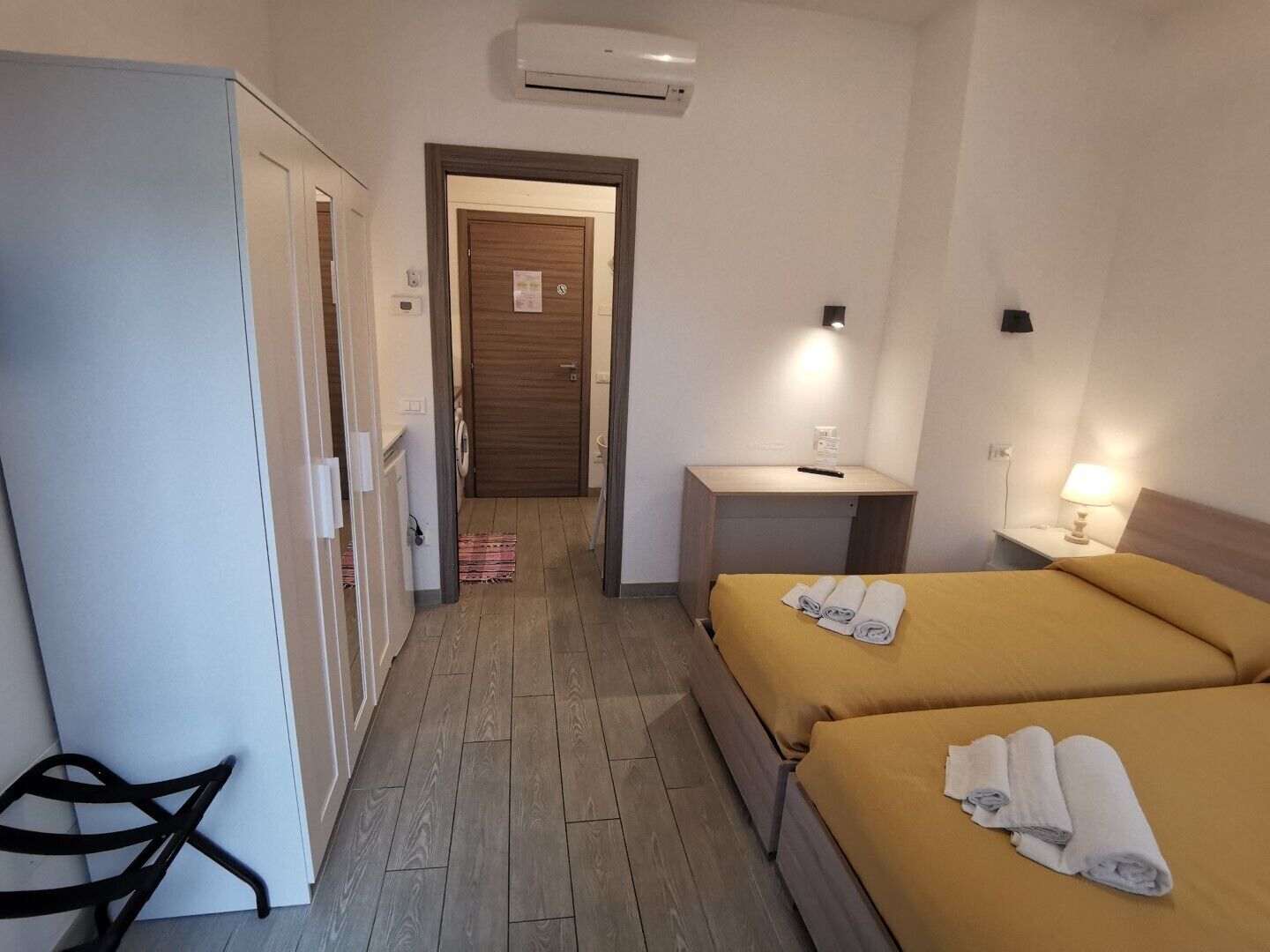 A hotel room with two beds, a desk, a chair, and a wardrobe.