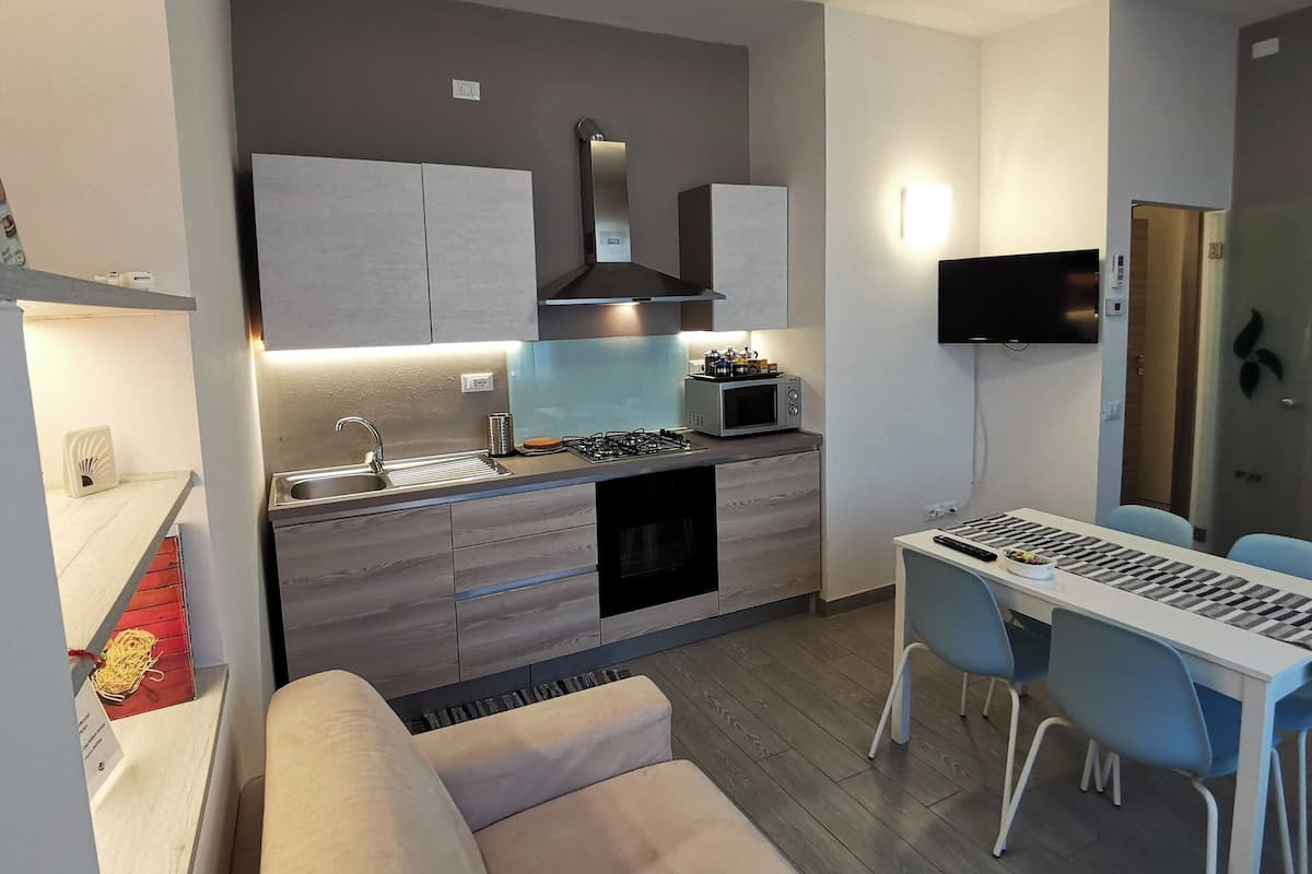 Eine moderne Küche mit Mikrowelle, Herd und Spüle. Ein Esstisch mit Stühlen und ein an der Wand befestigter Fernseher sind vorhanden.