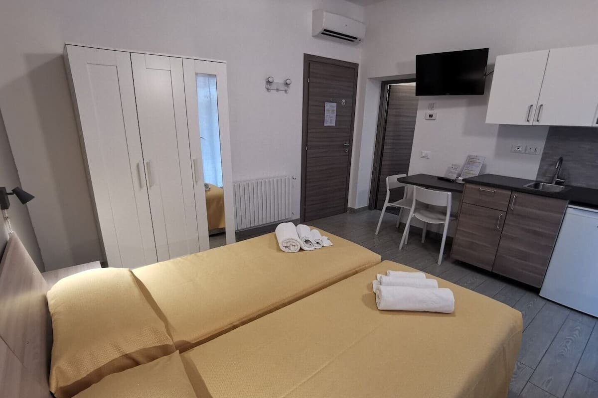 Ein Hotelzimmer mit Bett, Schreibtisch, Stuhl, einer Küchenzeile und einem Fernseher.