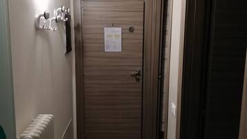 A hallway with a radiator, a wall-mounted air conditioner, a door with a notice, and a coat rack.