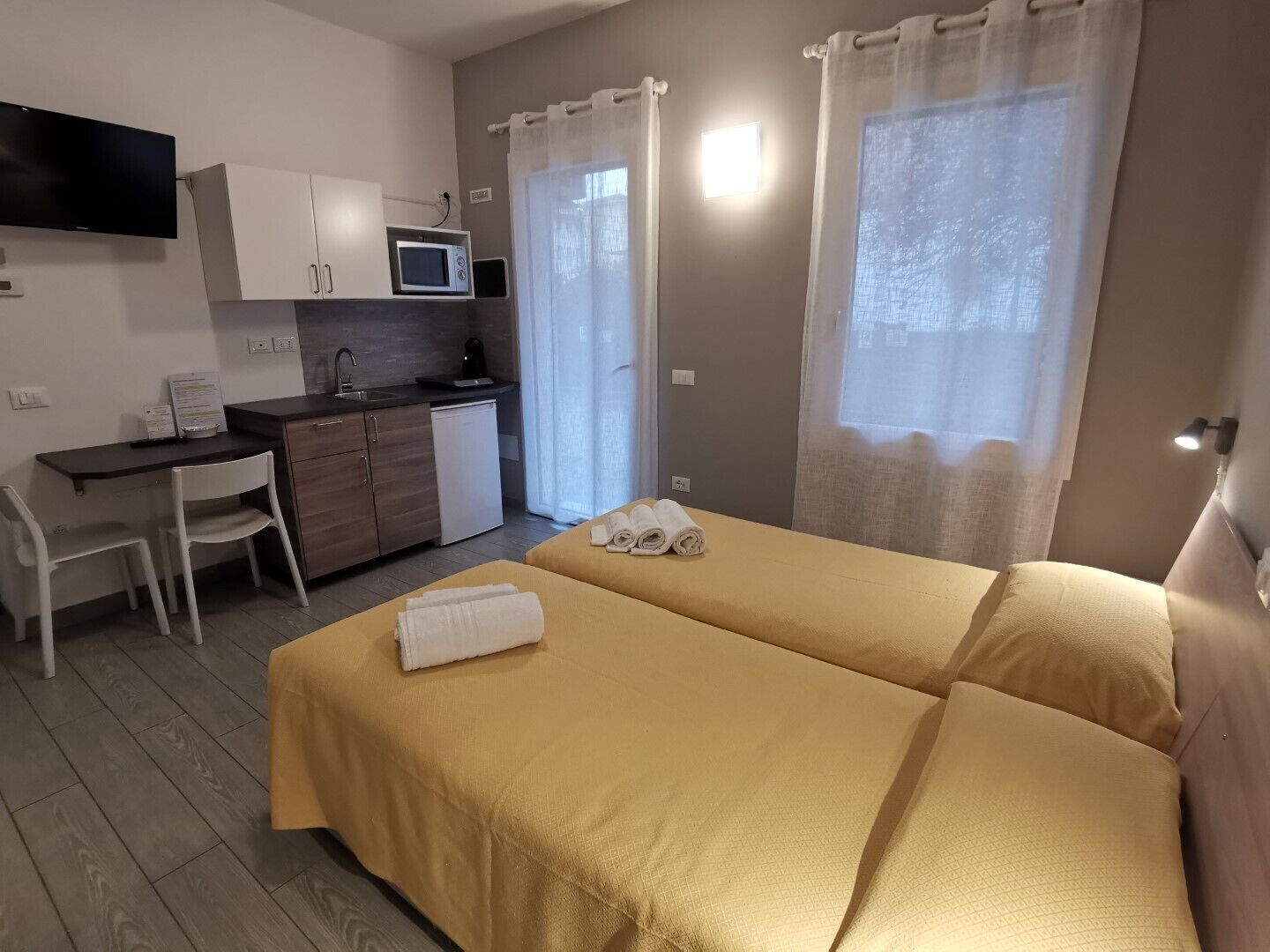 A compact hotel room with a bed, a desk, a microwave, and a small kitchenette.