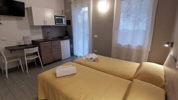 A compact hotel room with a bed, a desk, a microwave, and a small kitchenette.