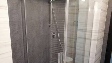 Un bany modern amb dutxa tancada amb vidre, rajoles fosques i un lavabo blanc.