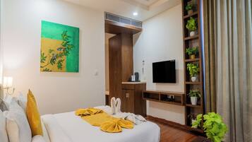 A hotel room with a bed, a TV, a desk, a wardrobe, and a plant shelf.