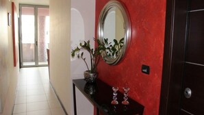 A hallway with a red wall, a mirror, a potted plant, and a console table with decorative items. - B&B Vescovo Rosso (Cosenza)