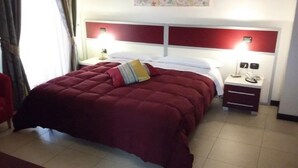 A hotel room with a queen-sized bed, a nightstand with a lamp, and a small table with a phone. - B&B Vescovo Rosso (Cosenza)