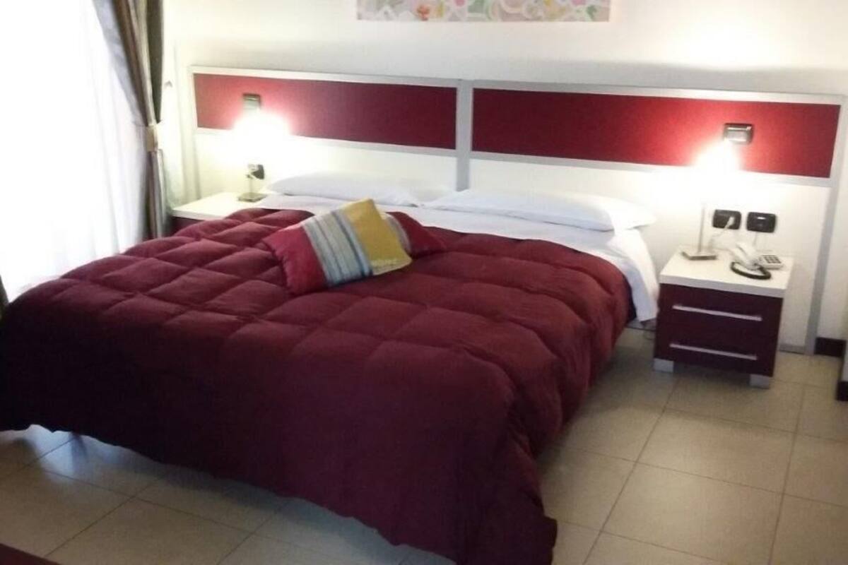 Une chambre d’hôtel avec un lit queen-size, une table de chevet avec une lampe et une petite table avec un téléphone.