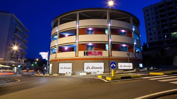 A multi-story building with a circular design, featuring balconies and illuminated signs. - B&B Vescovo Rosso (Cosenza)