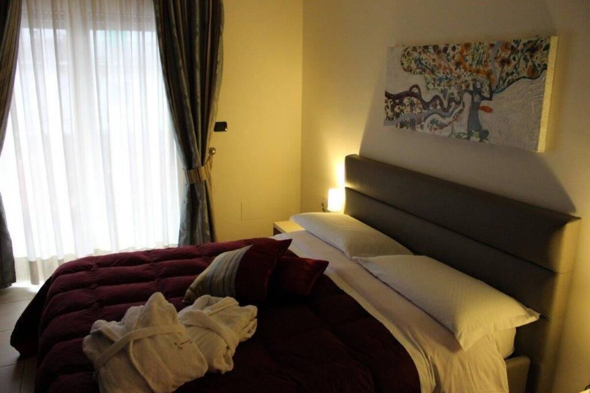 Une chambre d’hôtel avec un lit, une table de chevet, un tableau au mur et une fenêtre avec des rideaux.