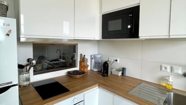 Una cocina moderna con armarios blancos, un microondas negro, una cafetera y un fregadero.