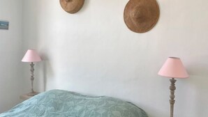 Un dormitorio con una cama, dos lámparas fijadas a la pared y dos sombreros tejidos en la pared.