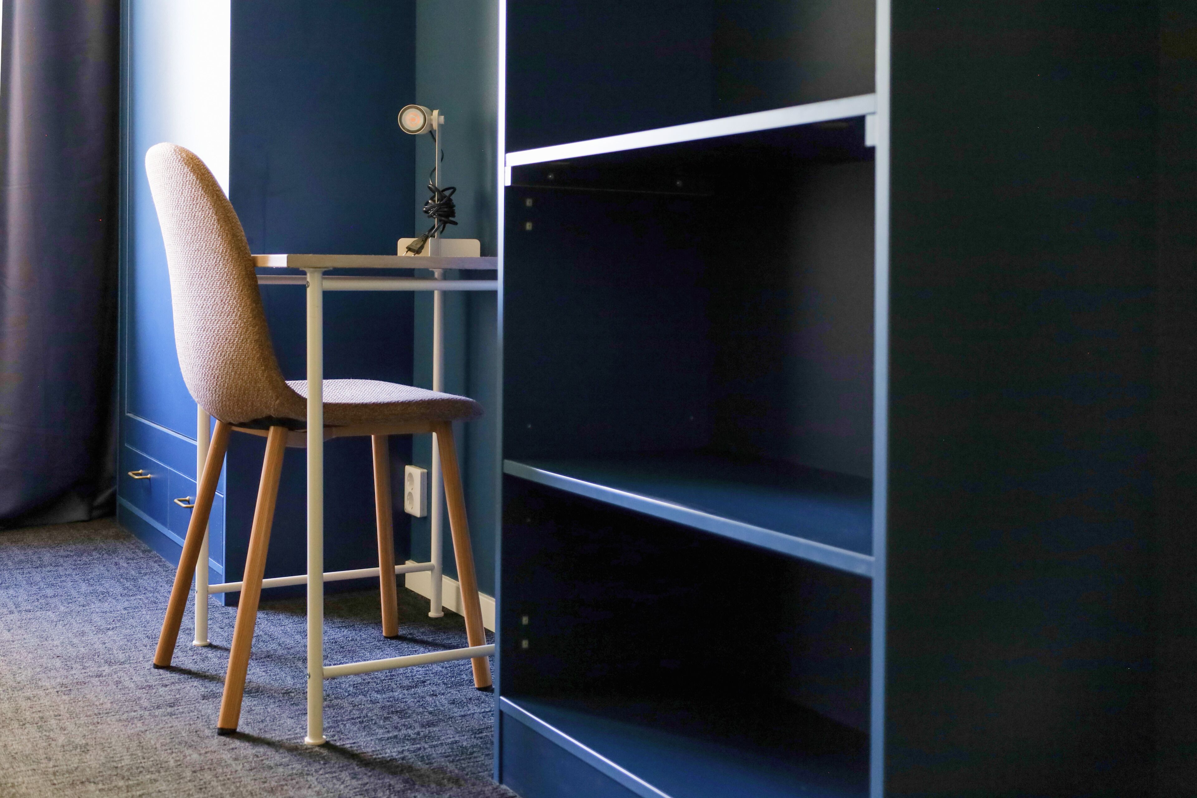 A room with a blue wall, a wooden chair, and a desk with a lamp.