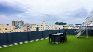 Eine Dachterrasse mit künstlichem Rasen, einem Esstisch mit Stühlen und einer Metalltreppe.