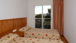 Ein Schlafzimmer mit hölzernem Kopfteil, einem Doppelbett mit blumigem Bettbezug, einem Nachttisch und einem großen Fenster mit Vorhängen.
