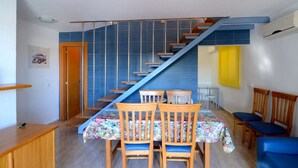 Ein Essbereich mit Treppe, Holzsesseln und einem Tisch mit floralem Tischläufer.