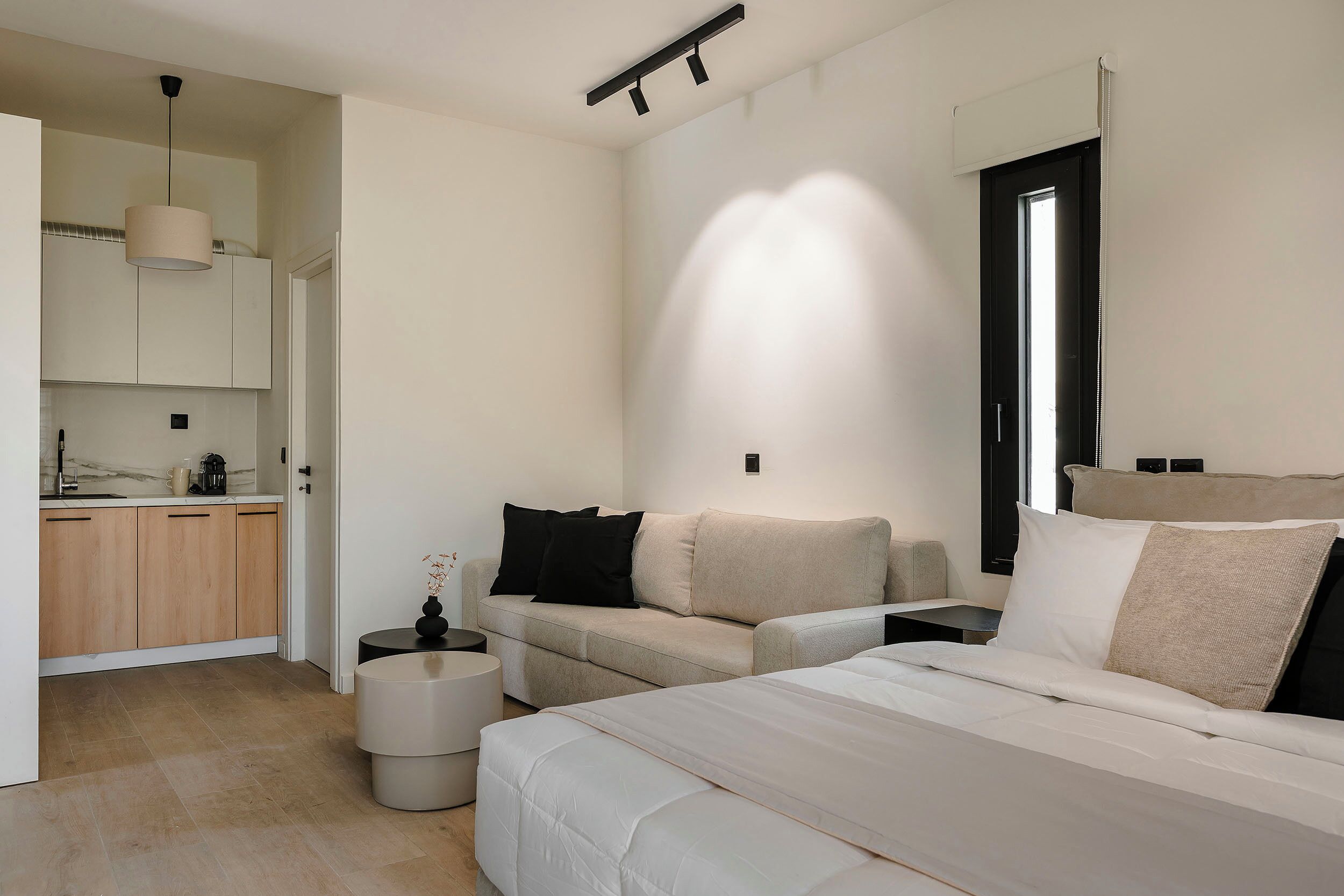 Une chambre à coucher moderne avec un lit, un canapé, une petite table et, au fond, un coin cuisine.