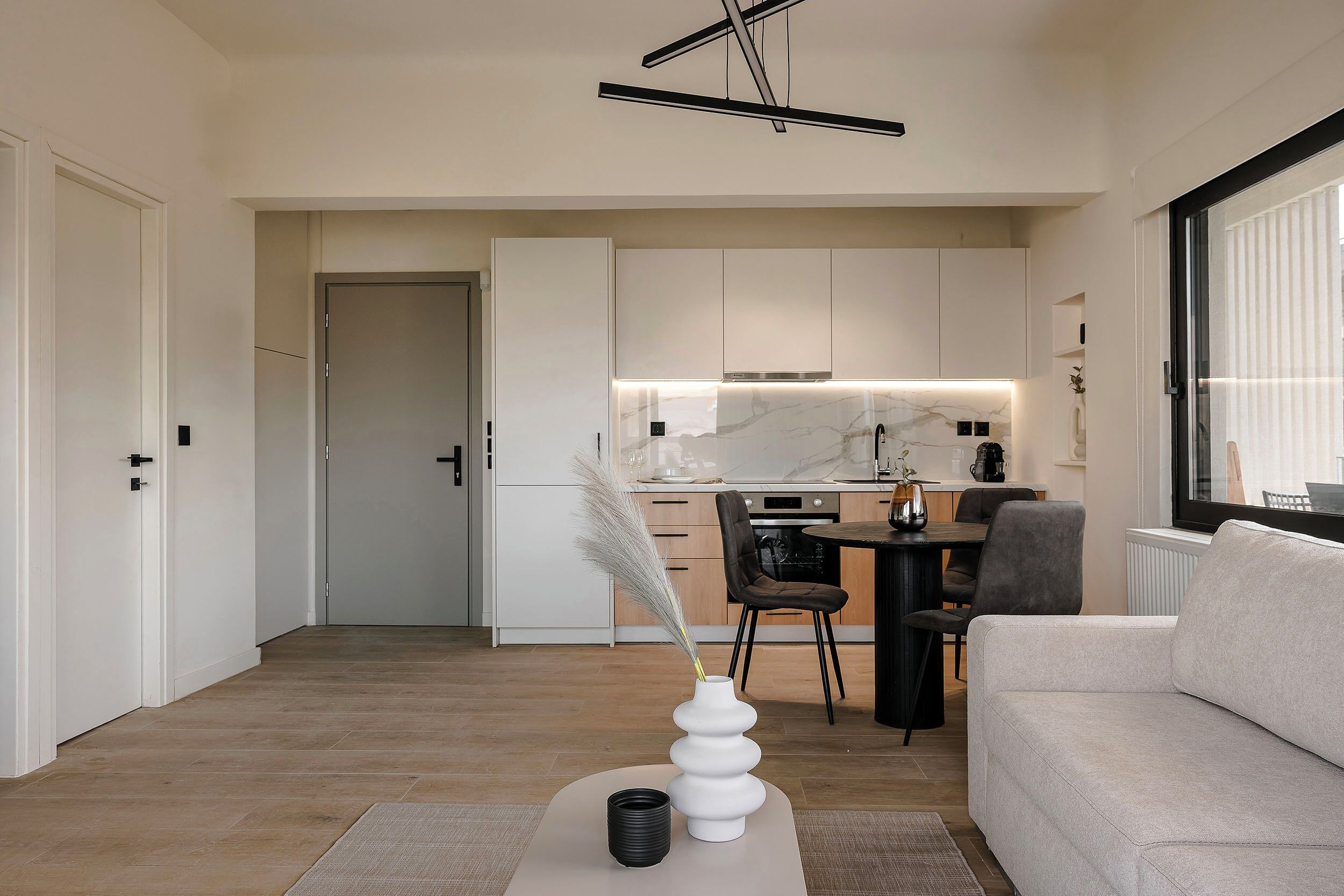 A modern living room with a sofa, a dining table with chairs, and a kitchen in the background.