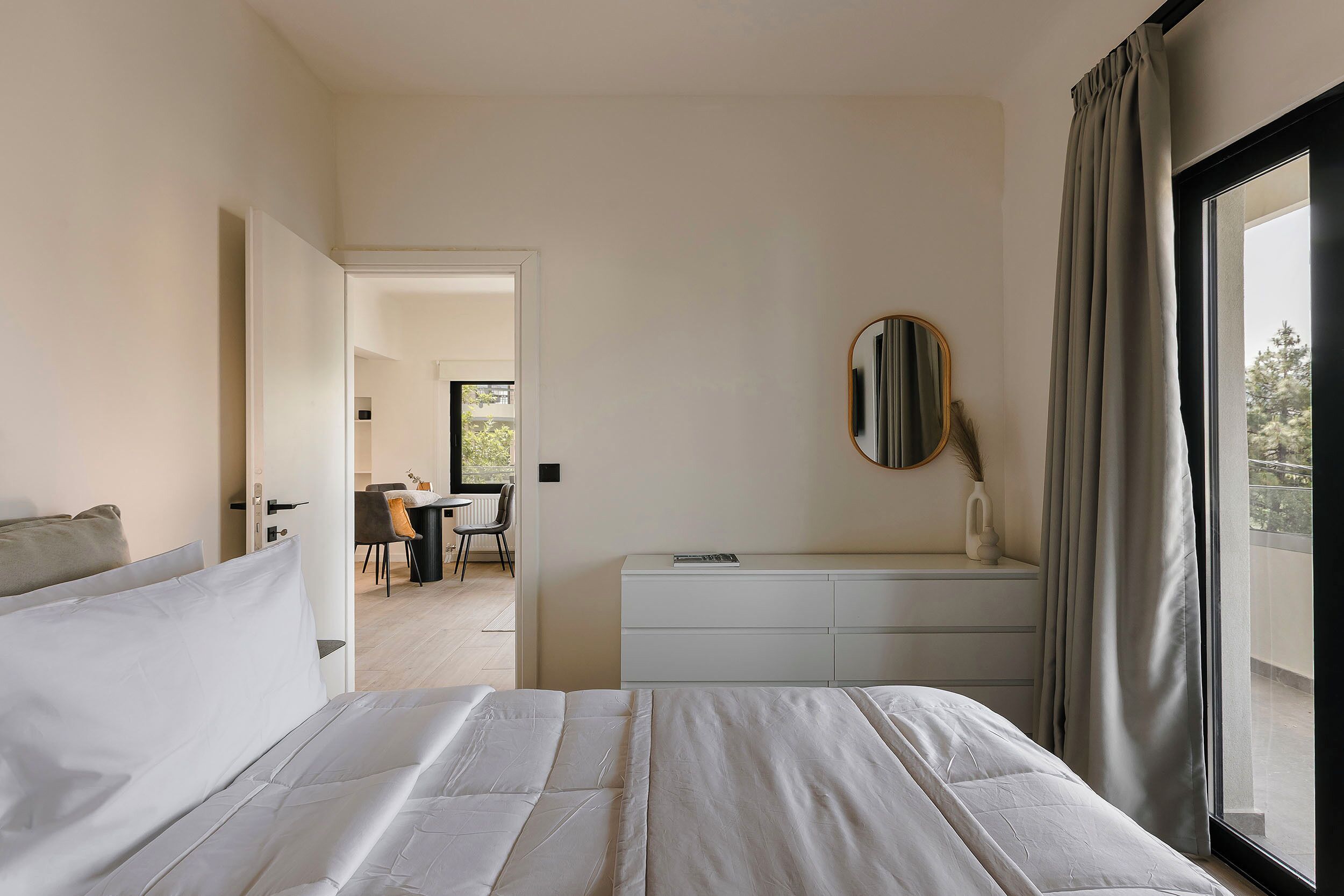 A bedroom with a bed, a dresser, a mirror, and a window with curtains.