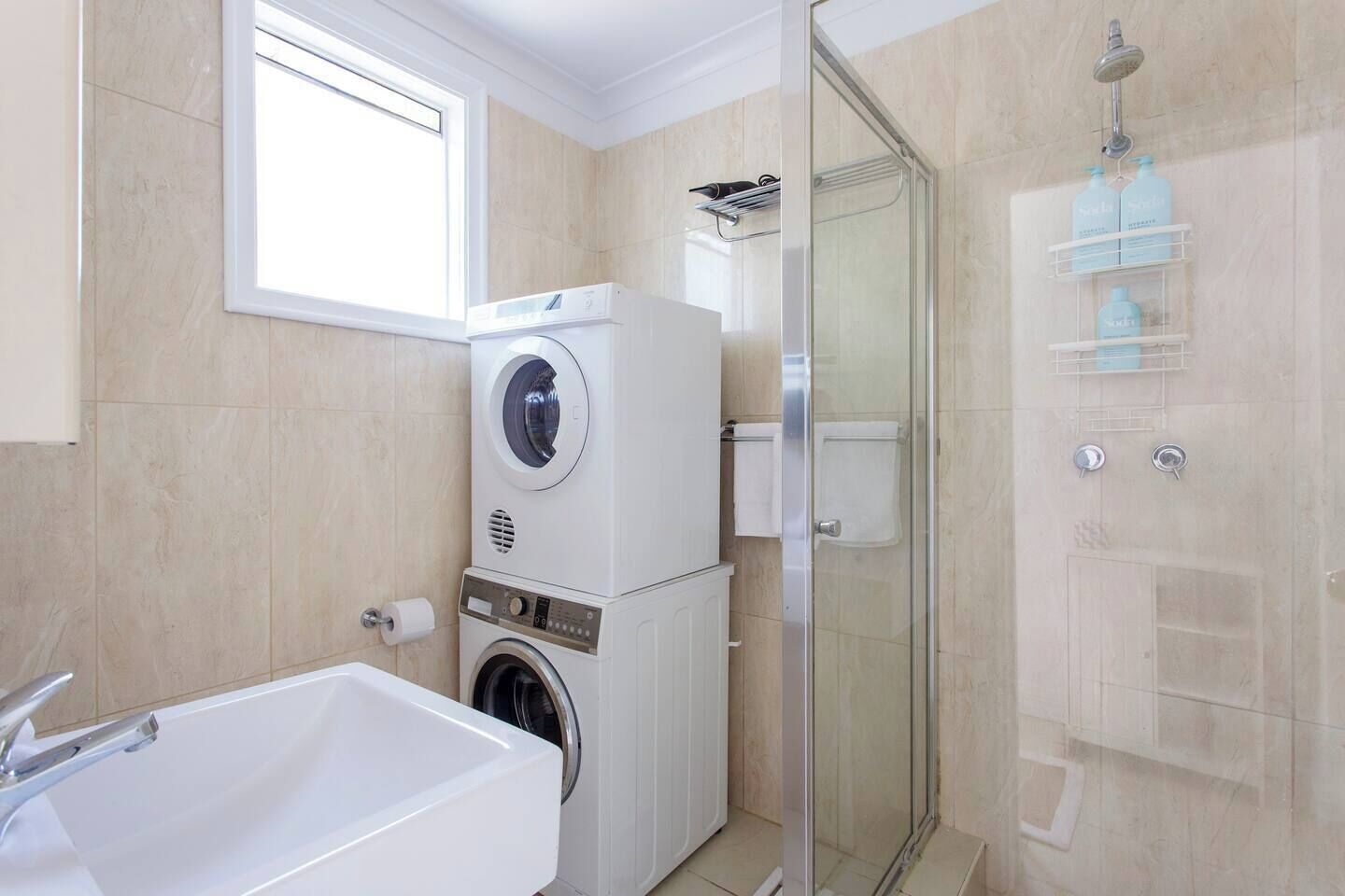 Ein modernes Badezimmer mit integrierter Waschmaschine und Trockner, einer Duschkabine aus Glas und einer großzügigen Badewanne.