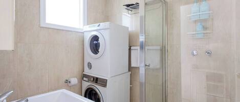 Ein modernes Badezimmer mit integrierter Waschmaschine und Trockner, einer Duschkabine aus Glas und einer großzügigen Badewanne.