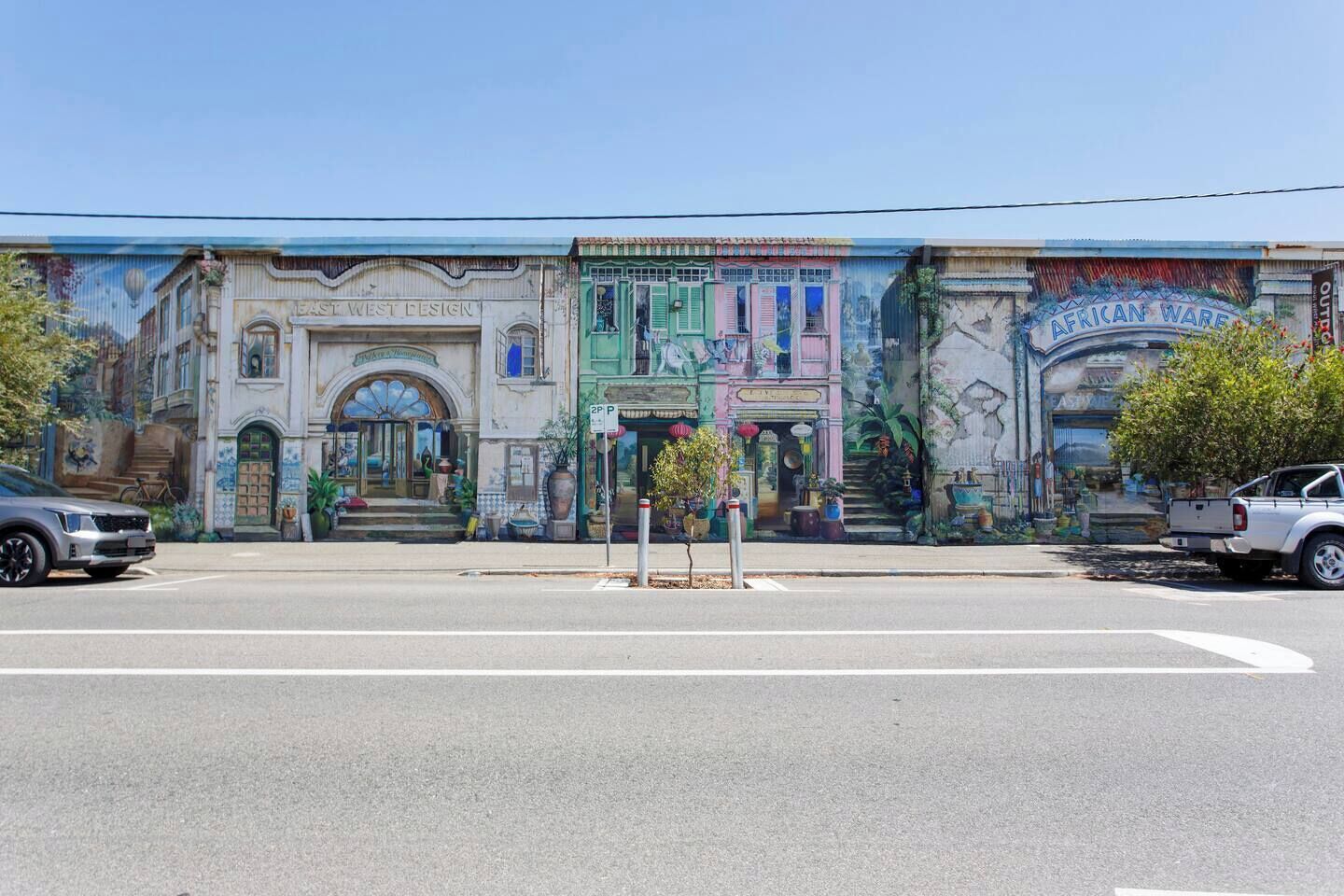 A street view with a mural on a building, a parking sign, and a street with cars.