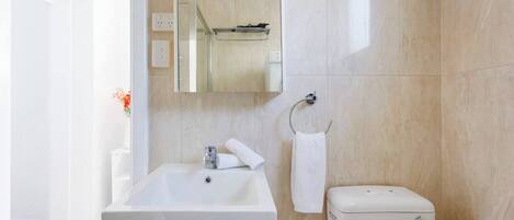 Un bagno con lavandino bianco, uno specchio, un portasciugamani e un water.
