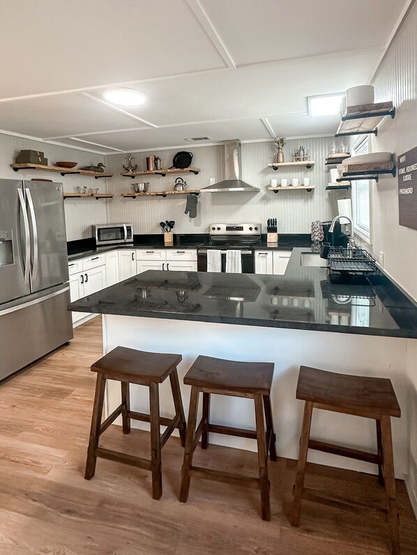 Una cocina moderna con una isla central, taburetes de madera, armarios blancos y un refrigerador de acero inoxidable.