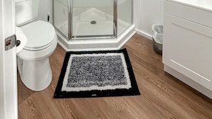 Un baño moderno con ducha acristalada, inodoro blanco, lavamanos con espejo y un pequeño estante con una planta.
