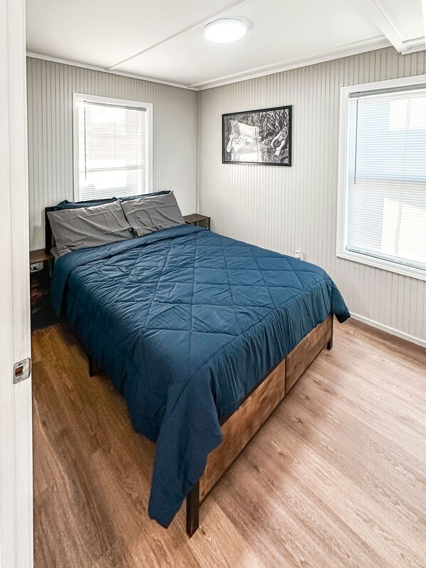 A bedroom with a bed, wooden floor, and a picture on the wall.