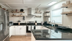 Una cocina moderna con una isla central, suelo de madera, armarios blancos y estanterías empotradas.