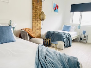 A bedroom with two beds, a brick wall, a hanging lamp, and a window with blinds.