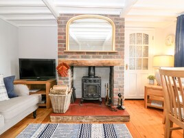 A cozy living room with a brick fireplace, a television, a sofa, and a wooden chair.