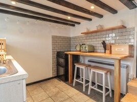 Una cocina con encimera de madera, dos taburetes, horno empotrado y salpicadero de azulejos.