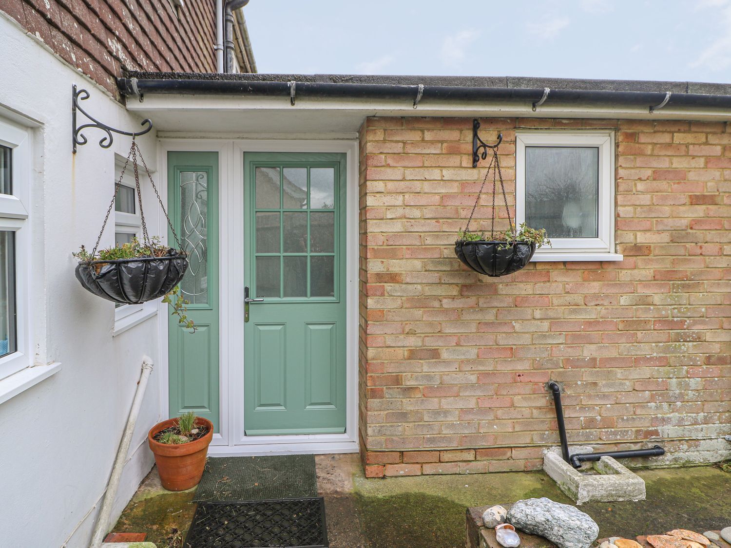 A house with a green door, two hanging flower baskets, a brick wall, and a window.
