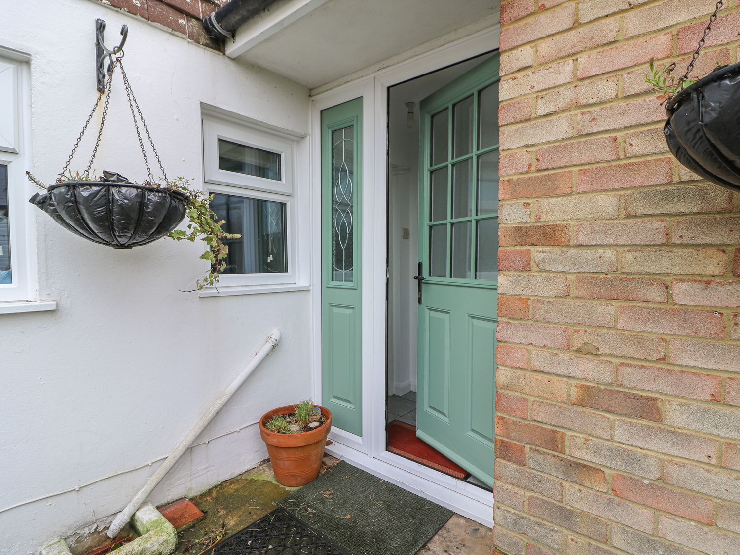 A narrow alleyway with a white wall, a green door, and a hanging black planter with plants.