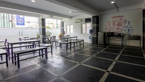 A spacious cafeteria with multiple tables and benches, large windows, and a wall with food-related illustrations. - Housr 84 Kondapur Near Botanical Garden (Hyderabad)