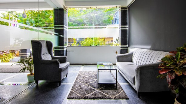 A modern living room with a sofa, armchair, and coffee table, a large window with a view of greenery, and a potted plant. - Housr 84 Kondapur Near Botanical Garden (Hyderabad)