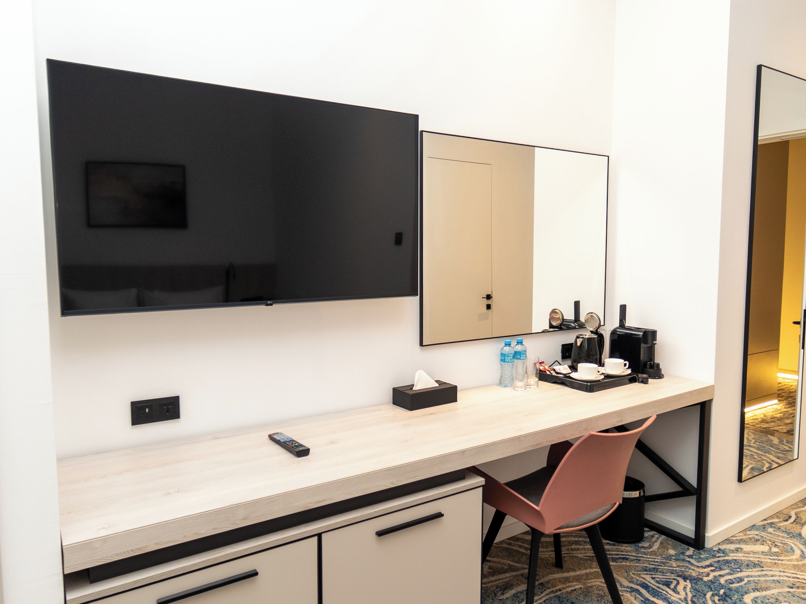 A hotel room with a desk, chair, and a large mirror.