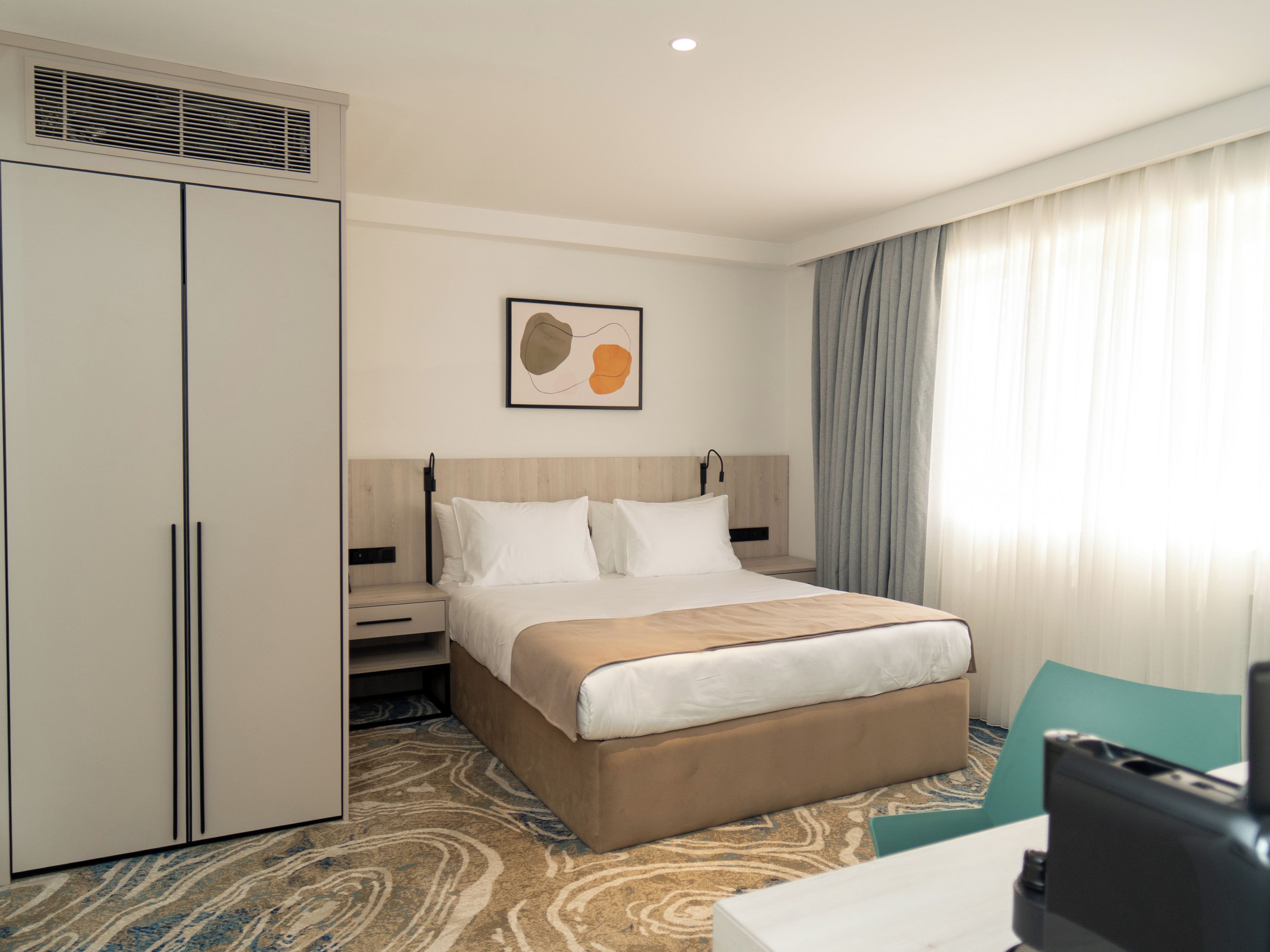 A hotel room with a bed, a wardrobe, a desk, and a chair.