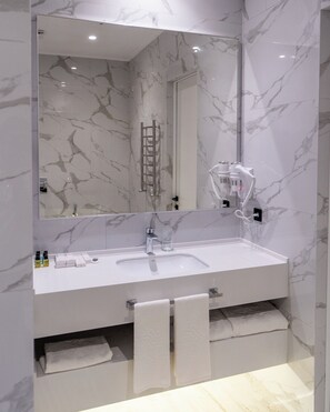 A modern bathroom with a marble backsplash, a large mirror, a white sink, and a towel rack.