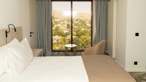 Habitación de hotel con una cama grande, una mesita pequeña y vistas de un pueblo a través de un ventanal amplio.