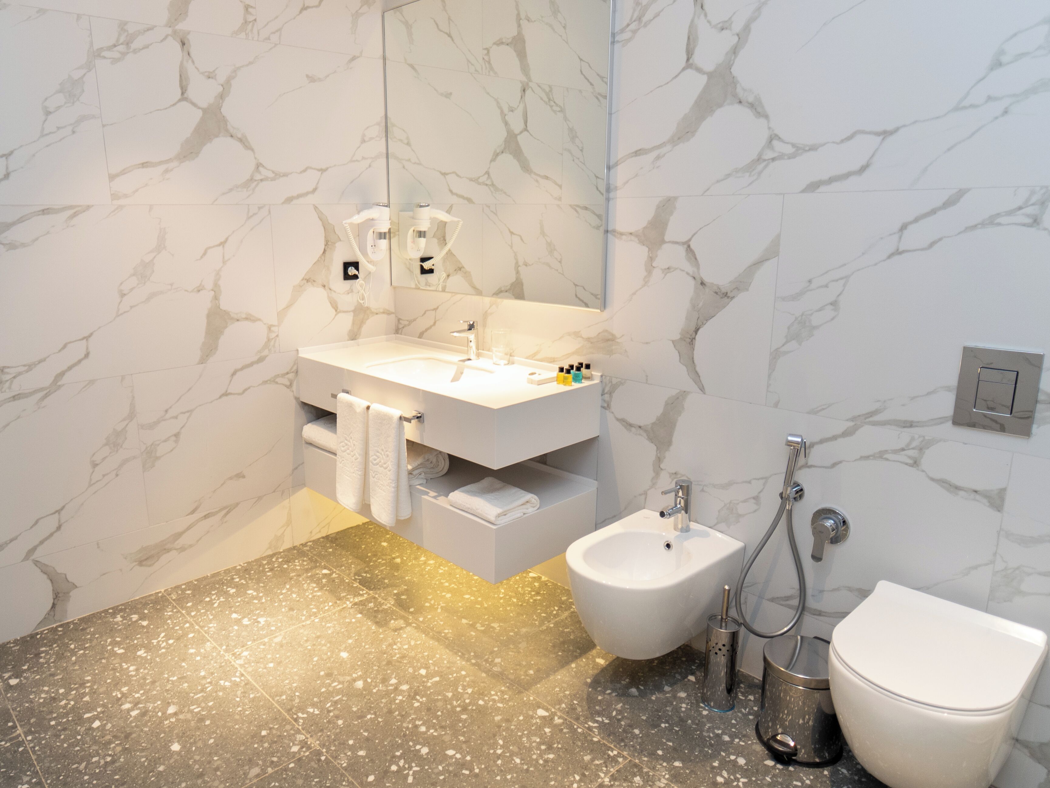 A modern bathroom with a marble wall, a white sink, a bidet, and a toilet.
