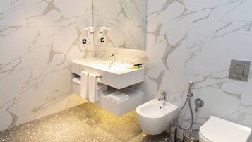 A modern bathroom with a marble wall, a white sink, a bidet, and a toilet.