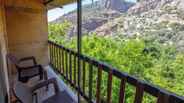 A balcony with two wicker chairs, overlooking a mountainous landscape with greenery and rocky terrain. - GÜL PENSİON (Fethiye)