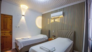A hotel room with two single beds, a wooden door, a wall-mounted air conditioner, and a ceiling light fixture. - GÜL PENSİON (Fethiye)