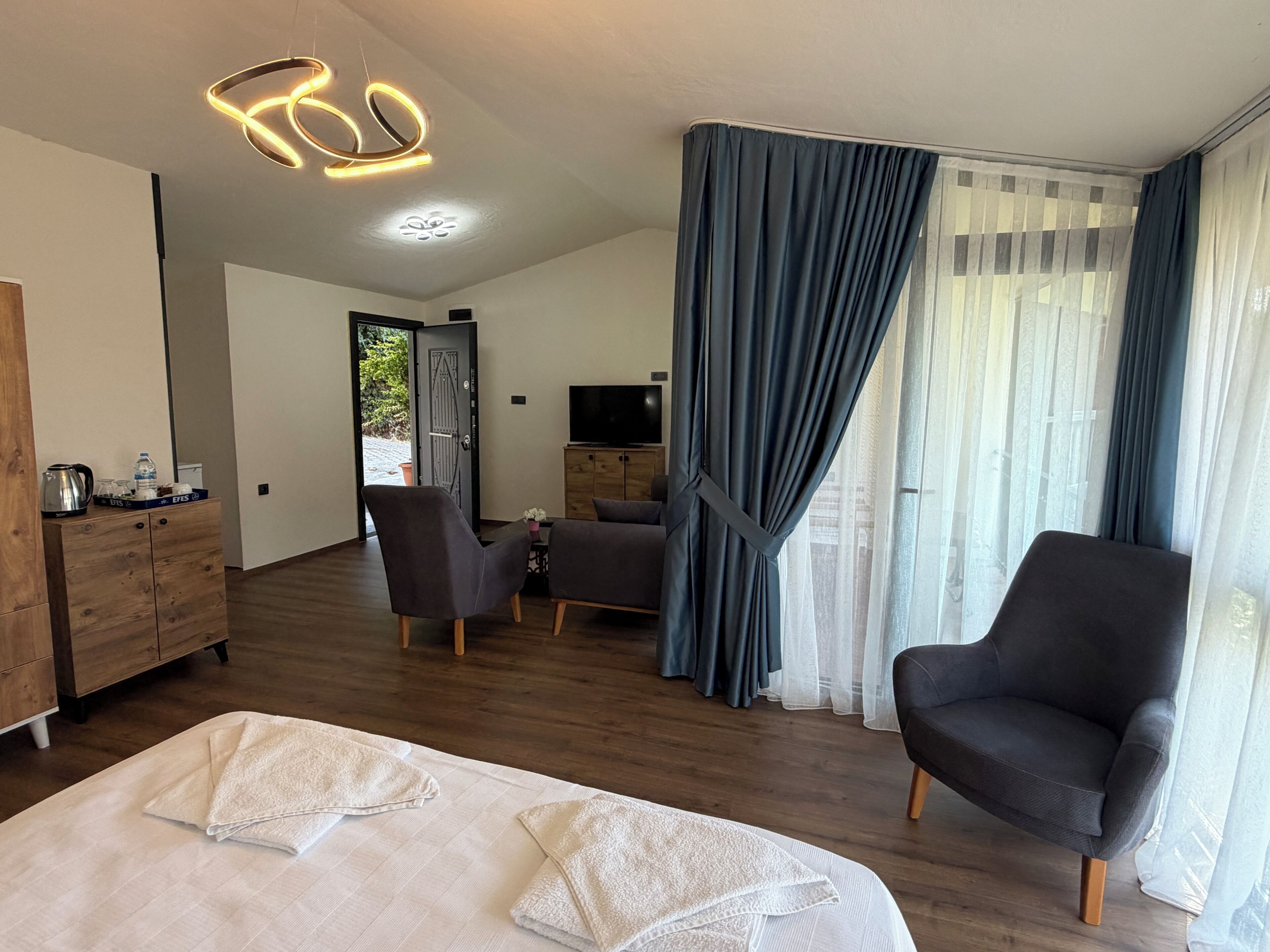 Ein Hotelzimmer mit einem Bett, zwei Sesseln, einem Fernseher und einer Holzkommode.